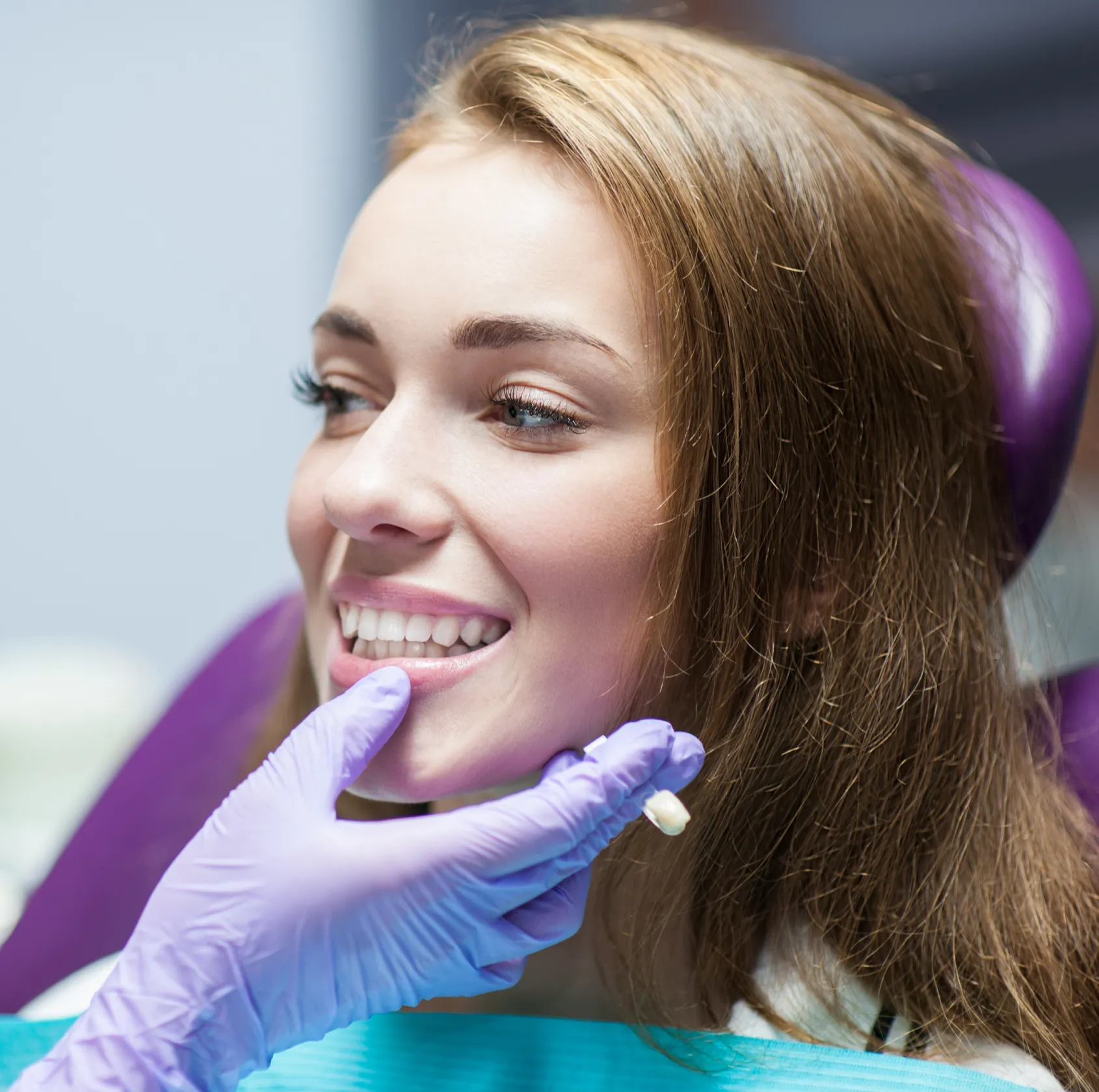 A dentist wearing gloves examines a smiling woman's teeth during a dental appointment.