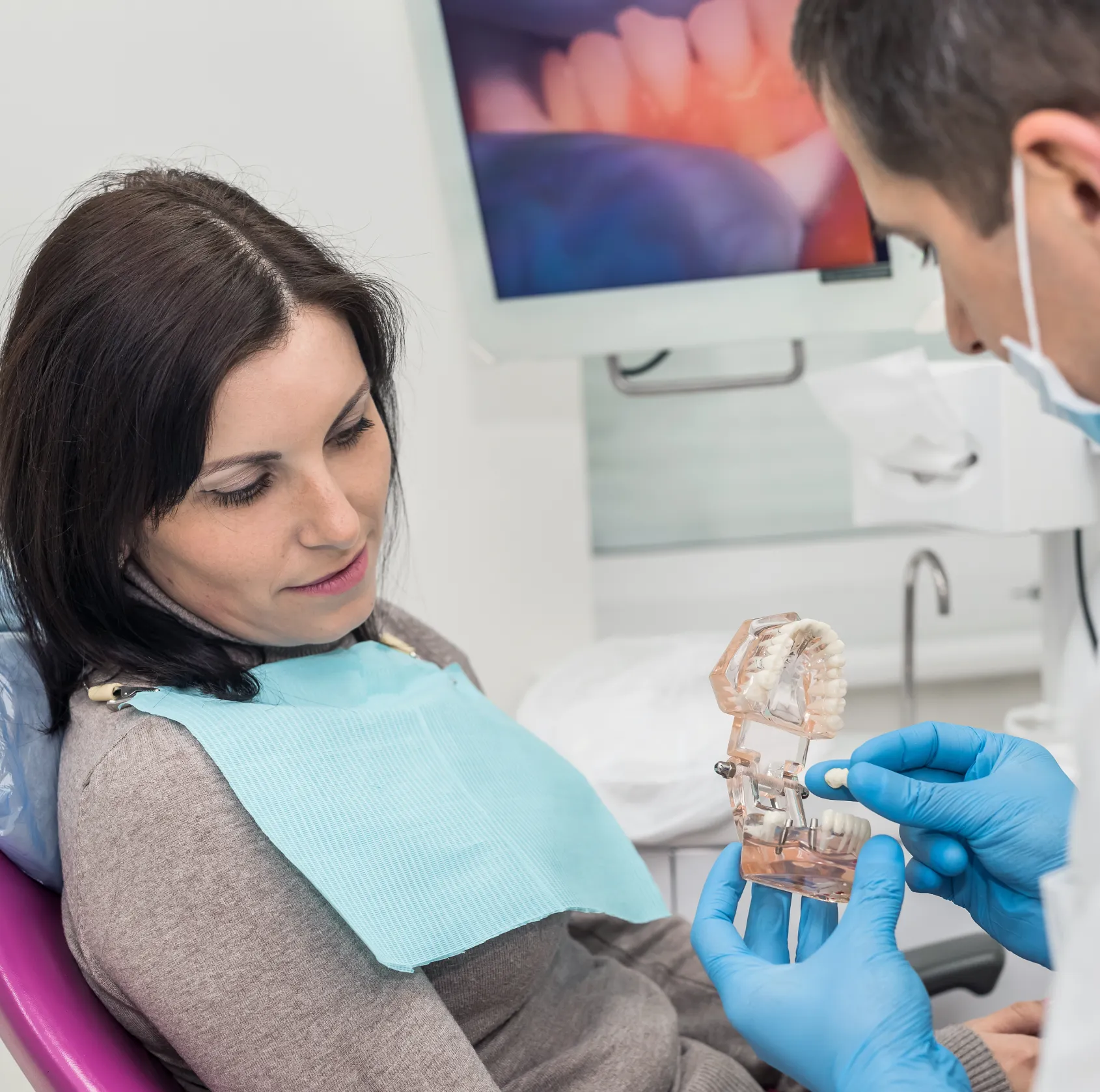 A dentist explains dental care to a patient using a tooth model in a clinic.