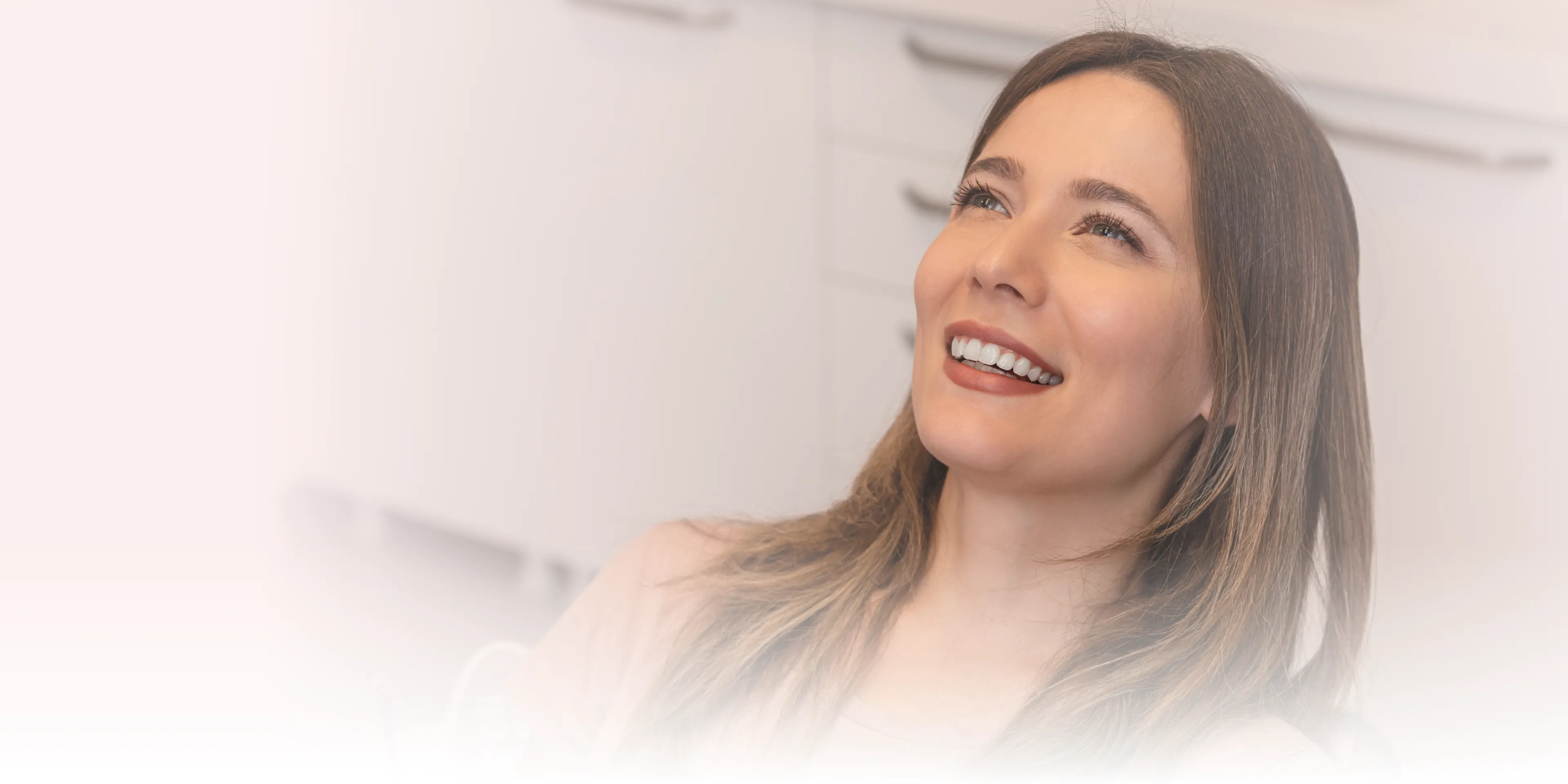 Smiling woman lying back in a dental chair, looking upwards in a bright dental office.