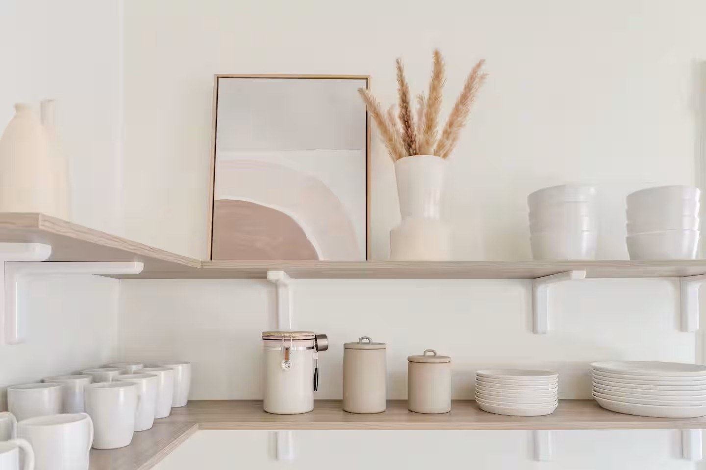 Minimalist kitchen shelves styled with white mugs, neutral canisters, stacked plates, pampas grass, and abstract desert artwork in a modern Tucson home.