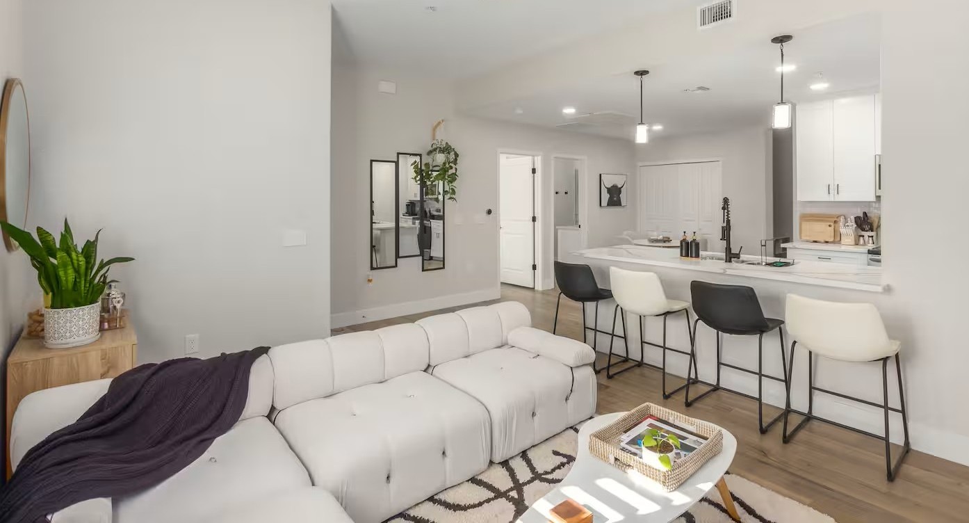 Bright modern living room and kitchen featuring a white sectional sofa, neutral decor, bar seating, and minimalist design in a Tucson vacation rental.