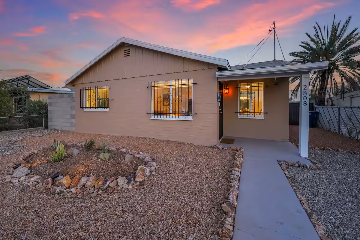 Single-story Tucson home with warm exterior lighting, desert landscaping, and a colorful sunset sky in the background.