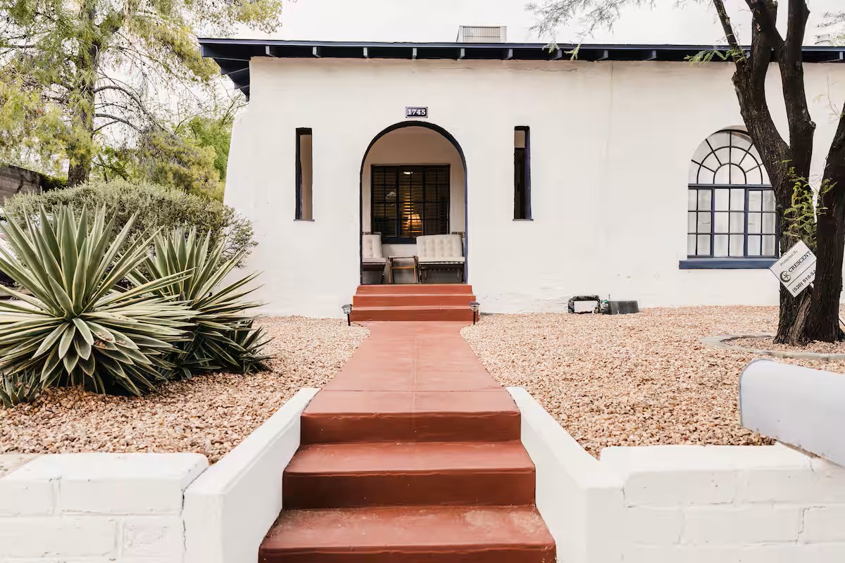 Classic white stucco home with arched entryway, terracotta steps, desert plants, and historic architectural details.