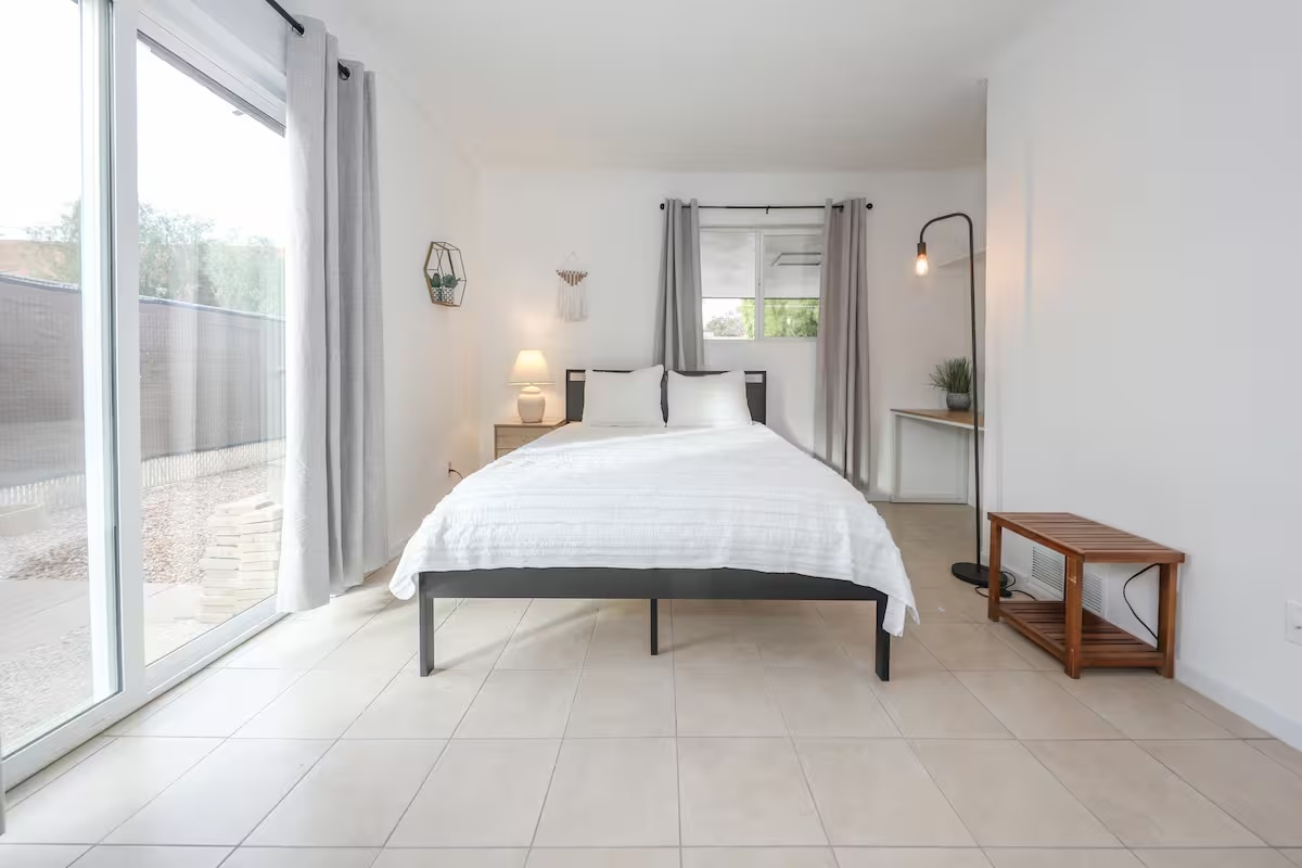 Spacious living room featuring large windows with desert views, light gray sofas, a grand piano, and warm wood flooring.