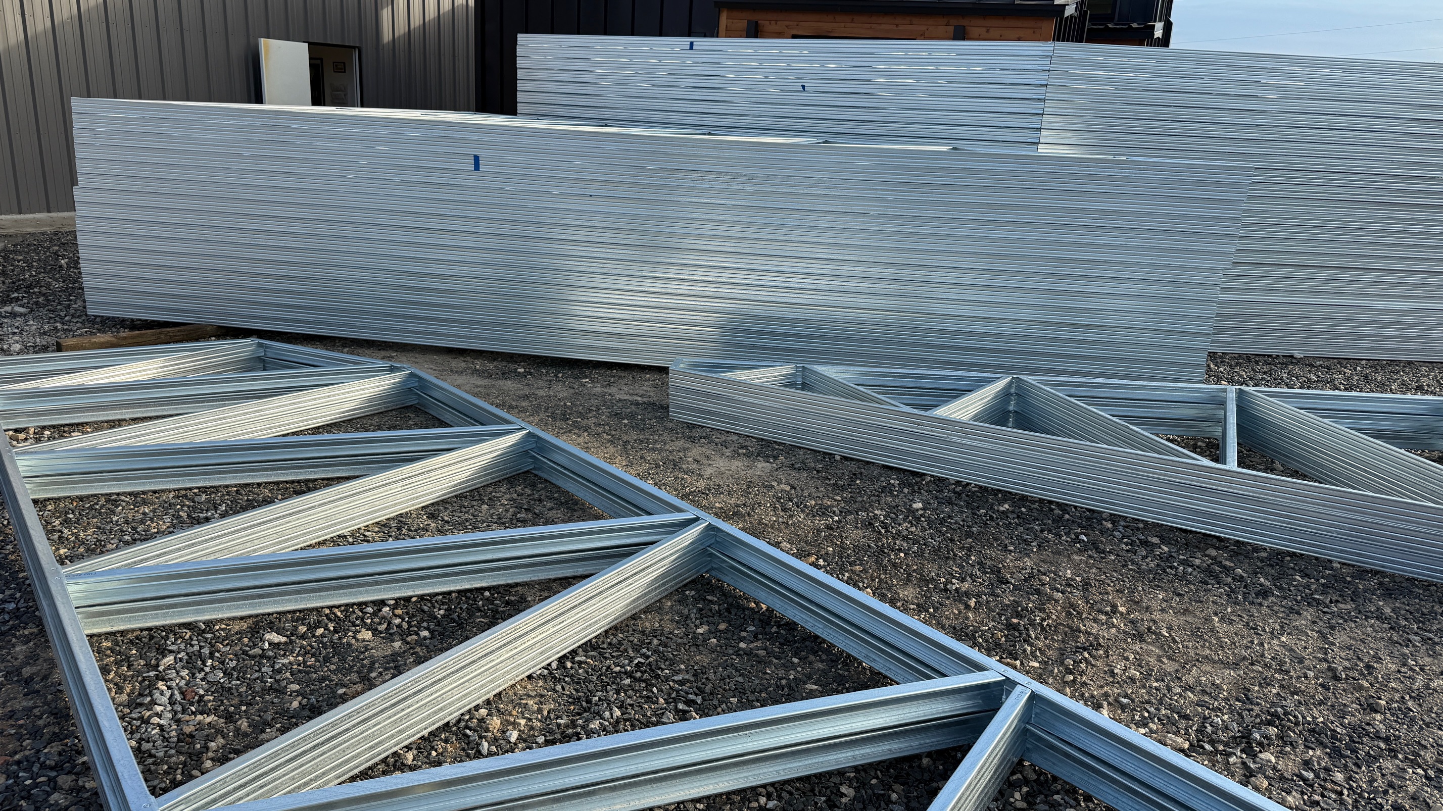Cold-formed steel trusses stacked and assembled at a jobsite before installation, showing prefabricated roof and floor truss components.