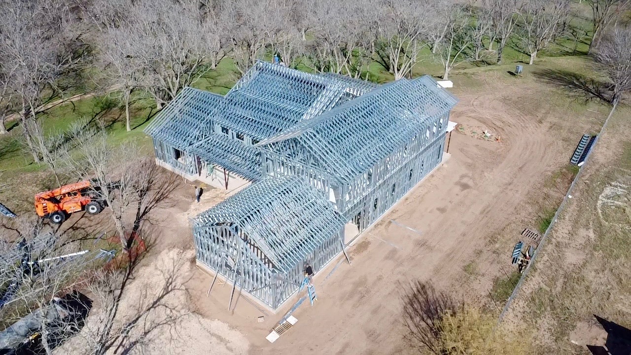 Aerial view of a custom home under construction with cold-formed steel wall framing and roof trusses installed on a large residential jobsite.