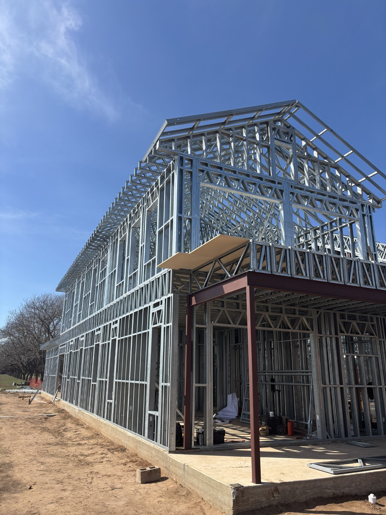 Tall custom home framed with cold-formed steel wall panels, steel roof trusses, and structural steel supports on a residential construction site.
