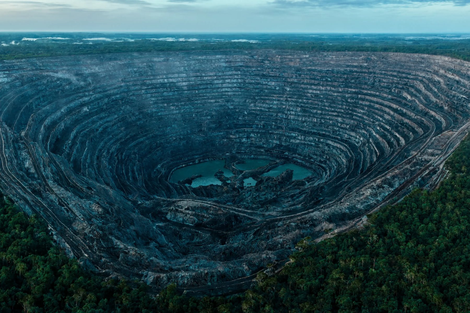 Vista aérea de mina de minério de ferro a céu aberto cercada por floresta ao amanhecer