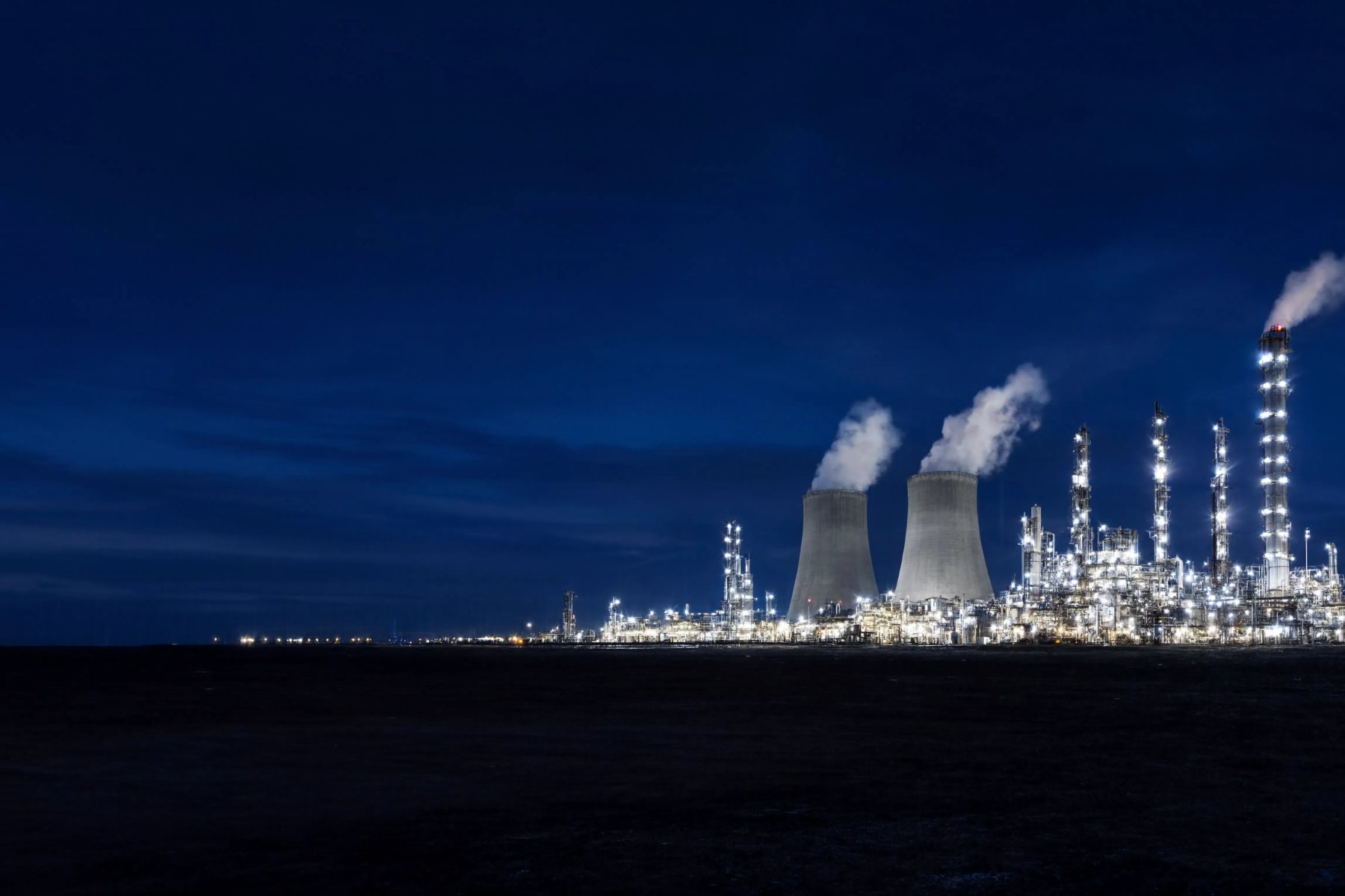 Refinaria e torres de resfriamento iluminadas sob o céu azul do anoitecer