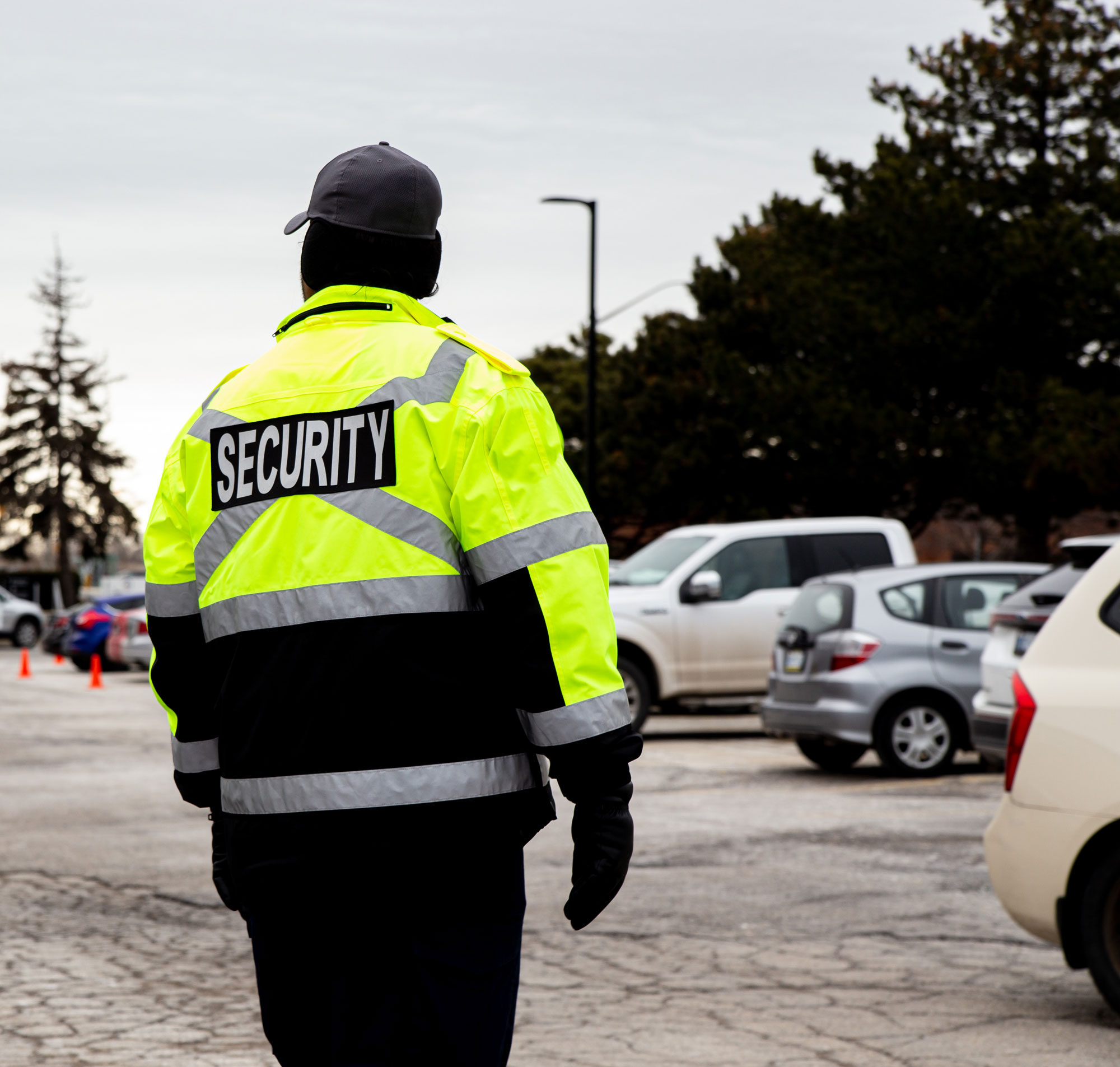Agent de sécurité de dos portant une veste jaune fluo avec le mot « SECURITY » sur le dos dans un stationnement.