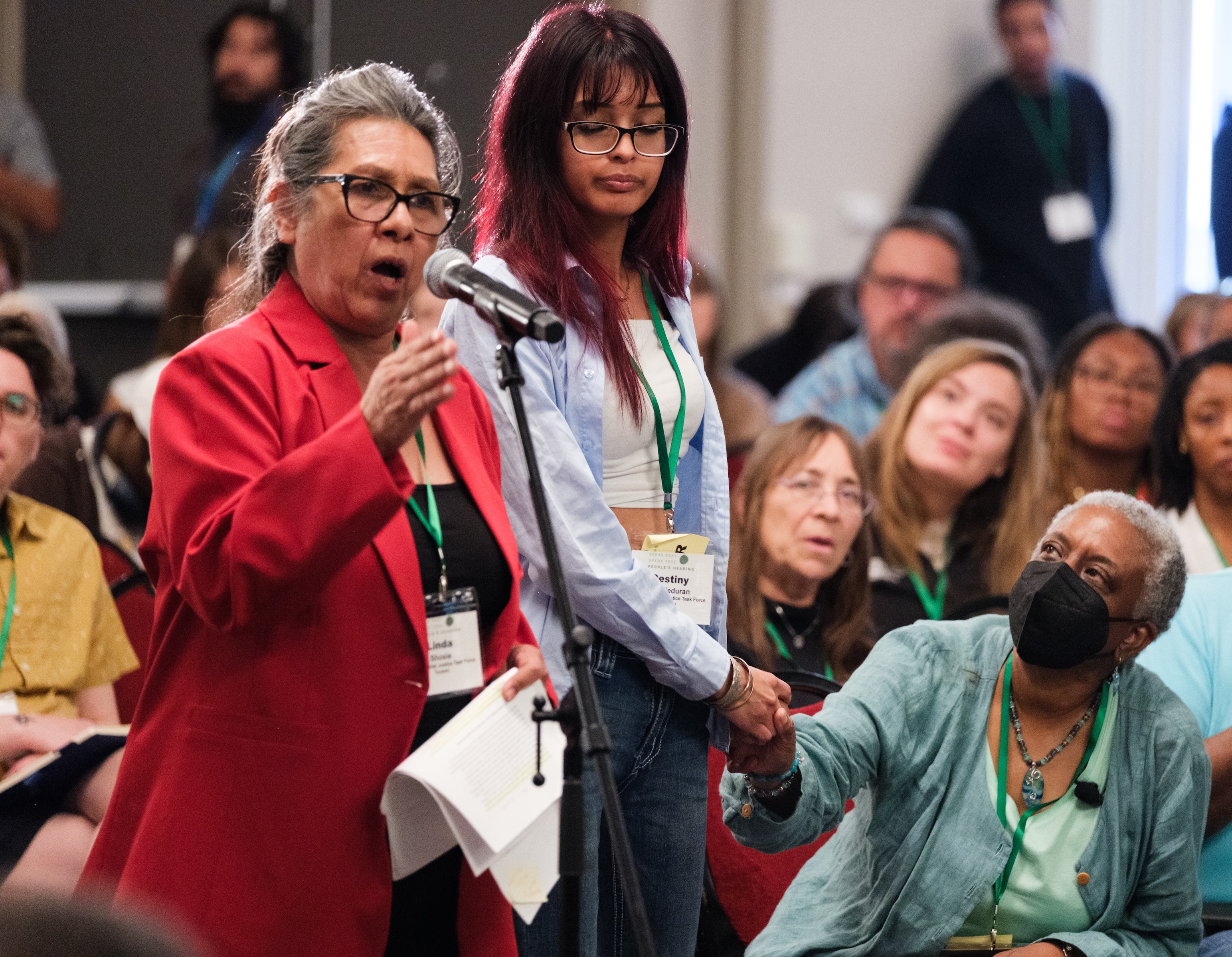 Woman in a red blouse standing and speaking at a convening