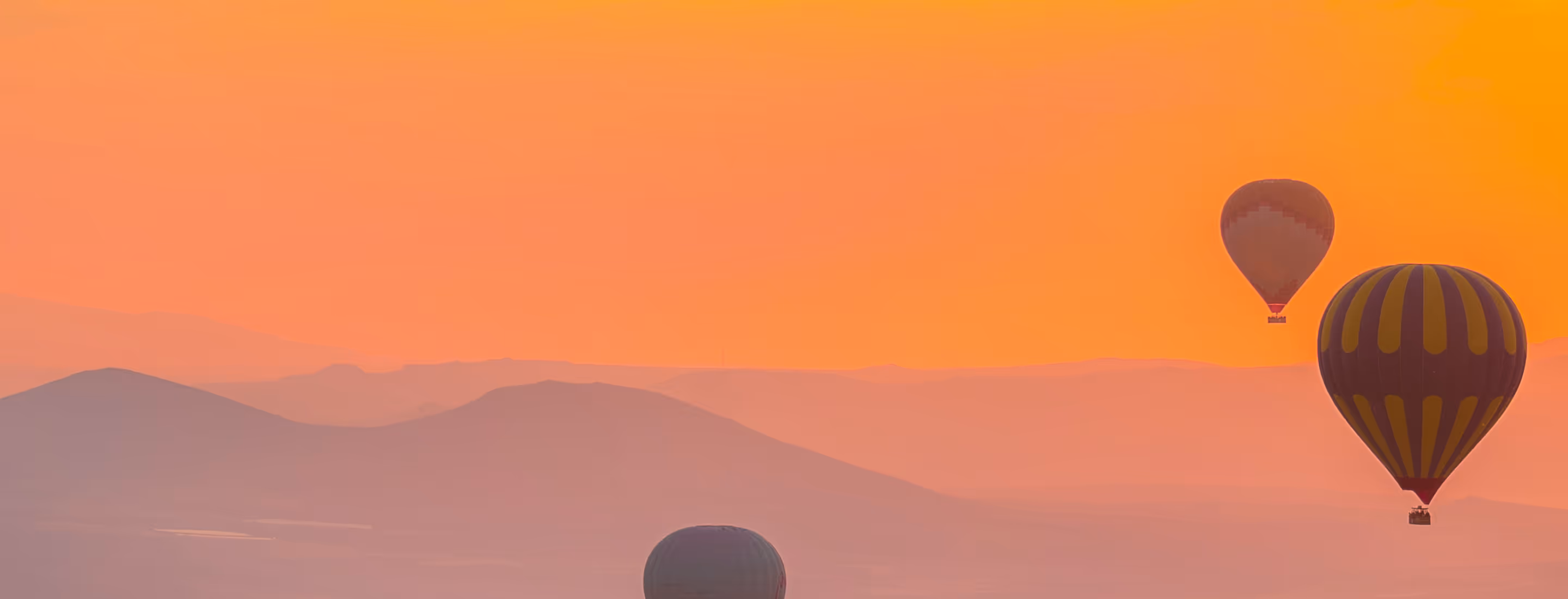 Hot air balloons floating at sunrise over mountains and valleys
