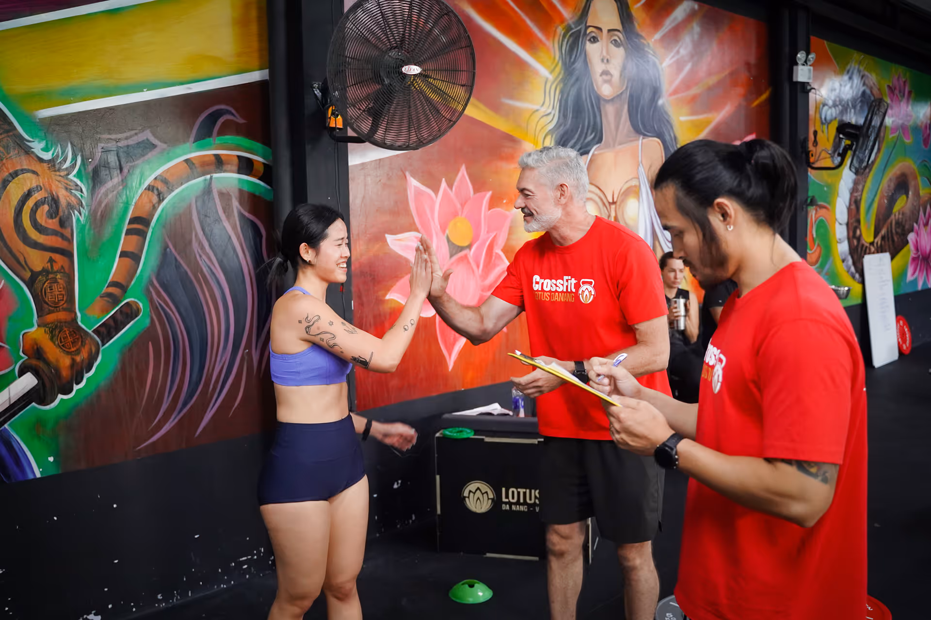 Woman in athletic wear giving a high-five to a man in a CrossFit shirt inside a gym with colorful mural walls.