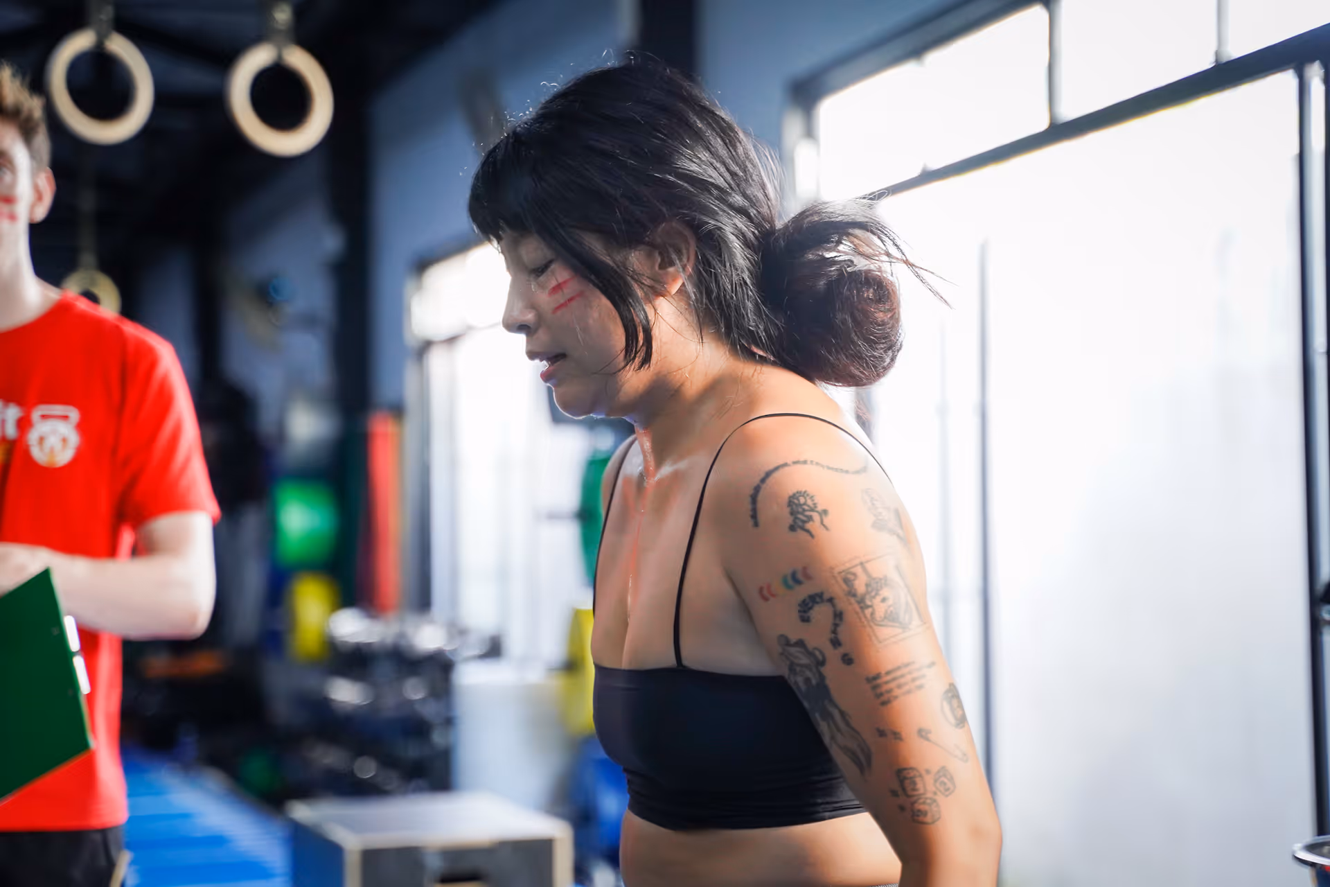 Woman with tattoos on her arm and red face paint lines working out intensely in a gym.