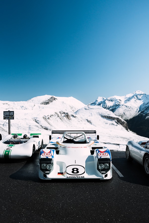 Three vintage race cars parked with snowy mountains behind.