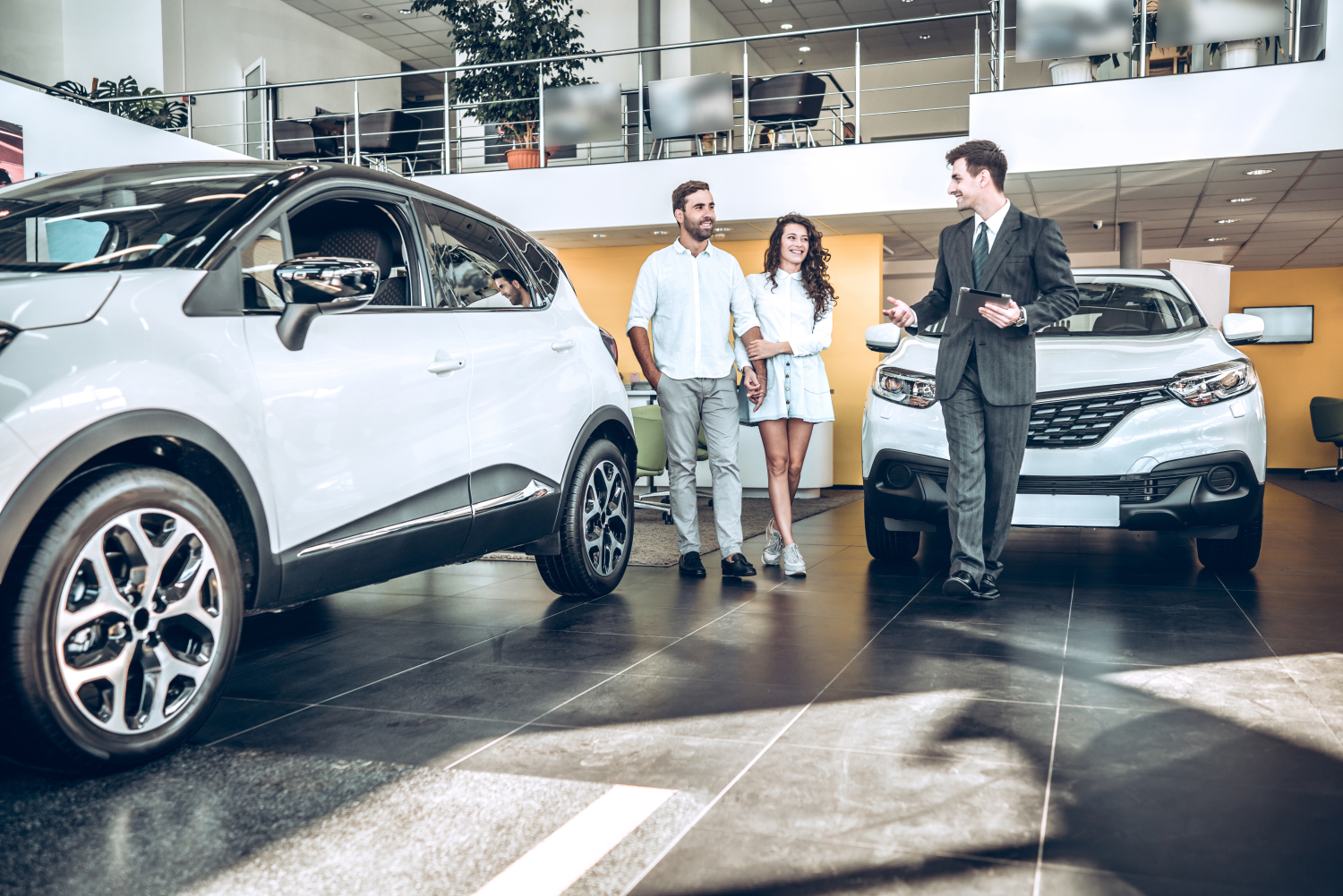 A couple shopping for a new car. Car dealer is walking them through a showroom.