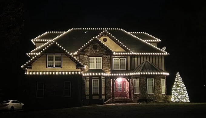 A house covered with white lights with a Christmas tree on the side.