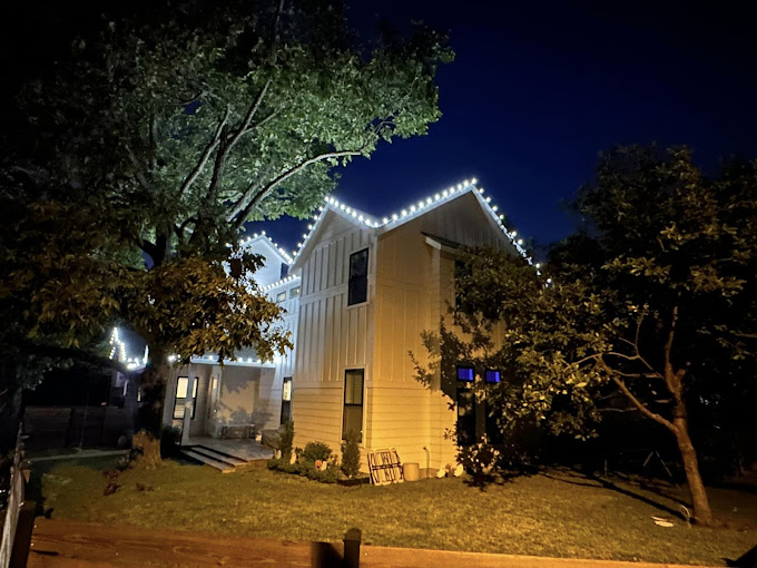 A house filled with white decorative Christmas lights, surrounded by a few trees.