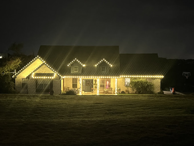 A house in a distance decorated with Christmas Lights.