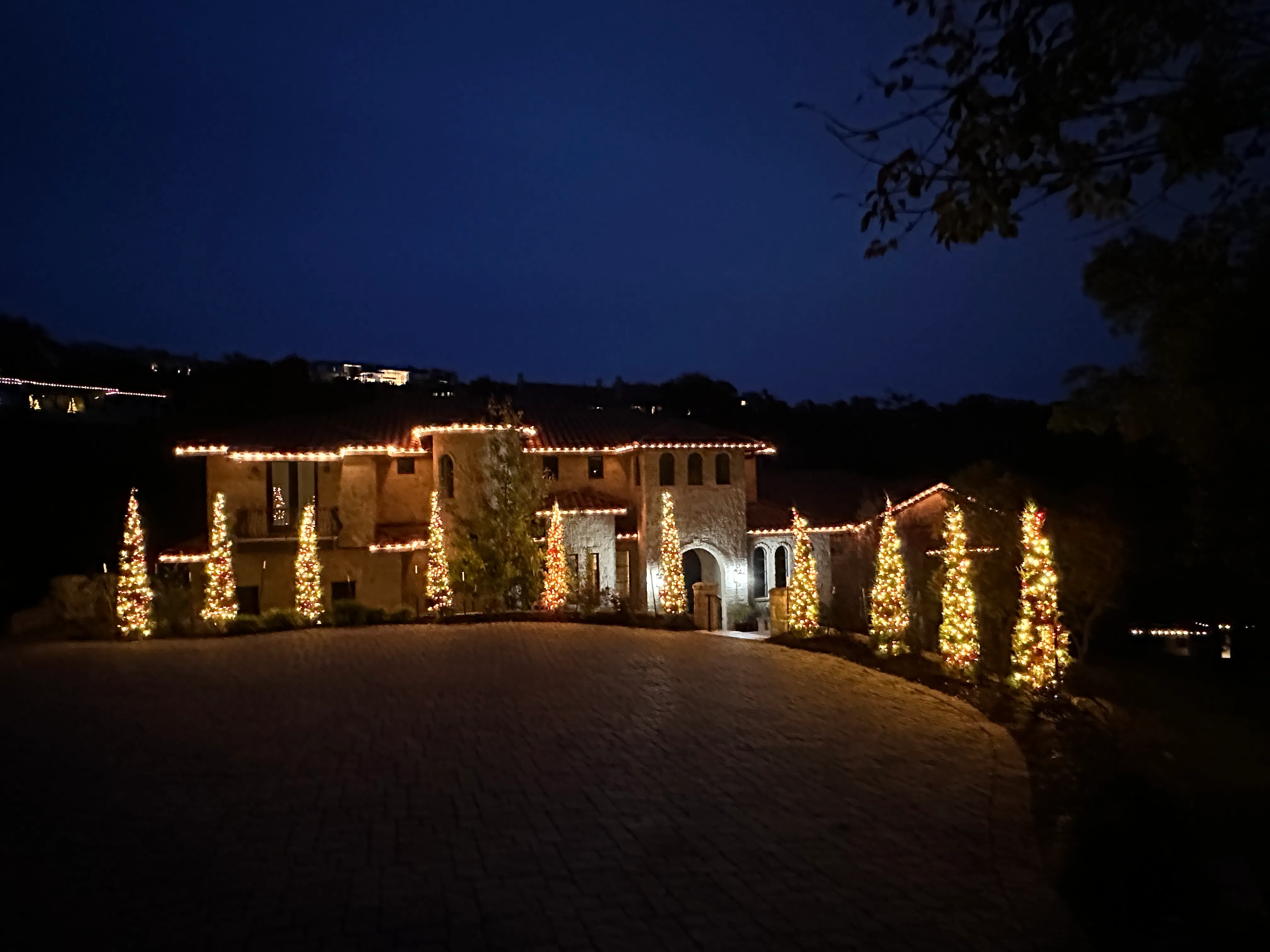 A house covered with Christmas lights with beautiful Christmas trees shining in the night.