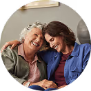 Ältere Frau und jüngere Frau lachen zusammen auf einem Sofa, wirken glücklich und entspannt.