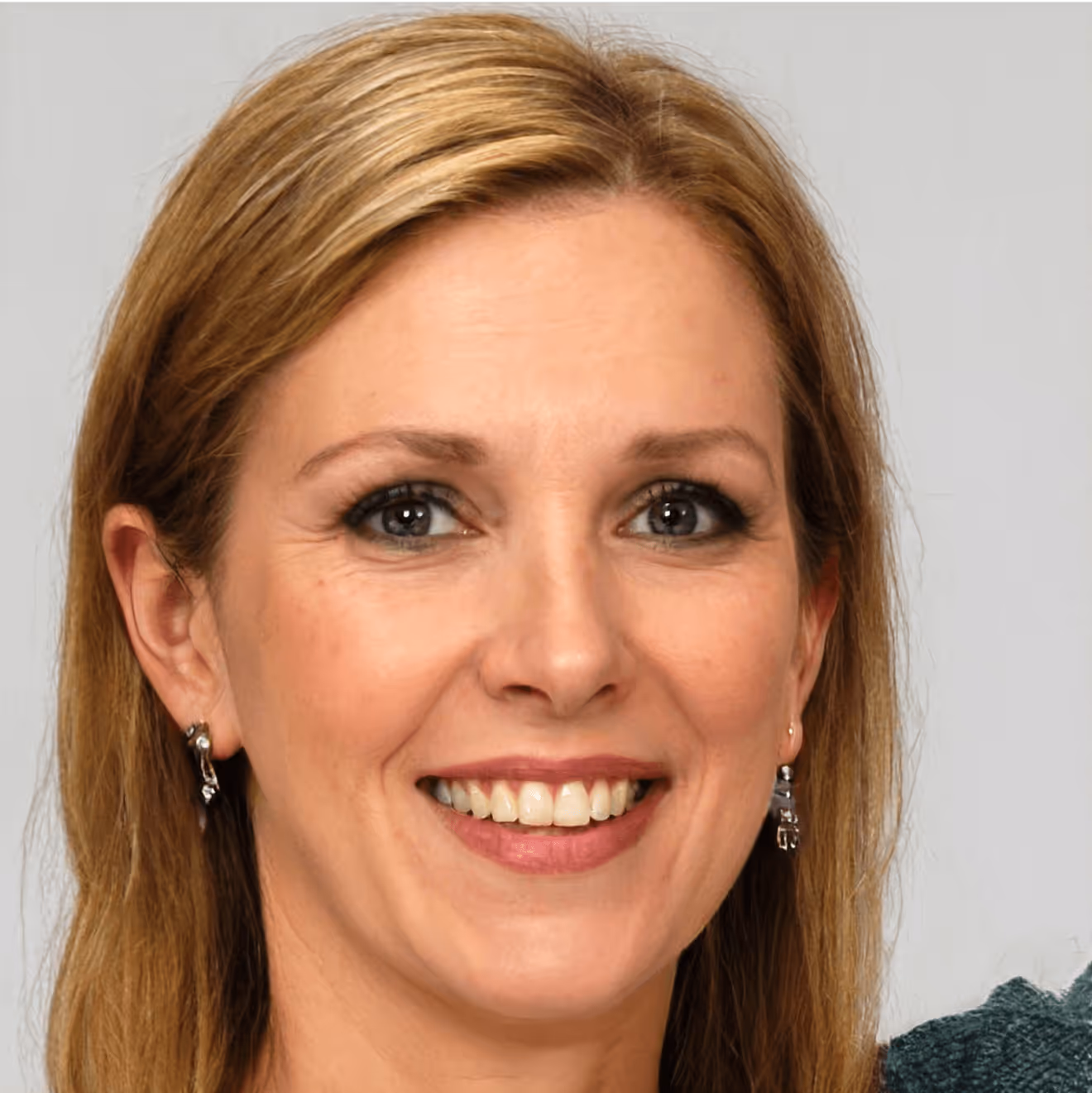 Freundliche lächelnde Frau mit blonden Haaren und Ohrringen vor neutralem Hintergrund.