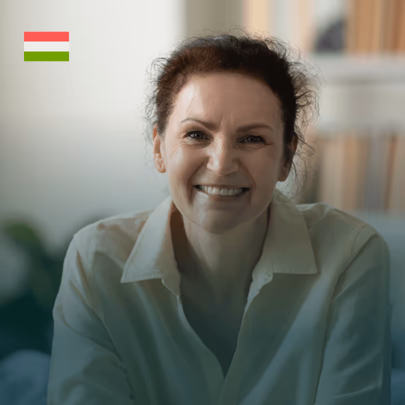 Lächelnde Frau in weißem Hemd vor Bücherregal, ungarische Flagge oben links.