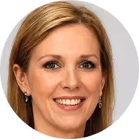 Lächelnde Frau mit langen blonden Haaren und Ohrringen vor neutralem Hintergrund.