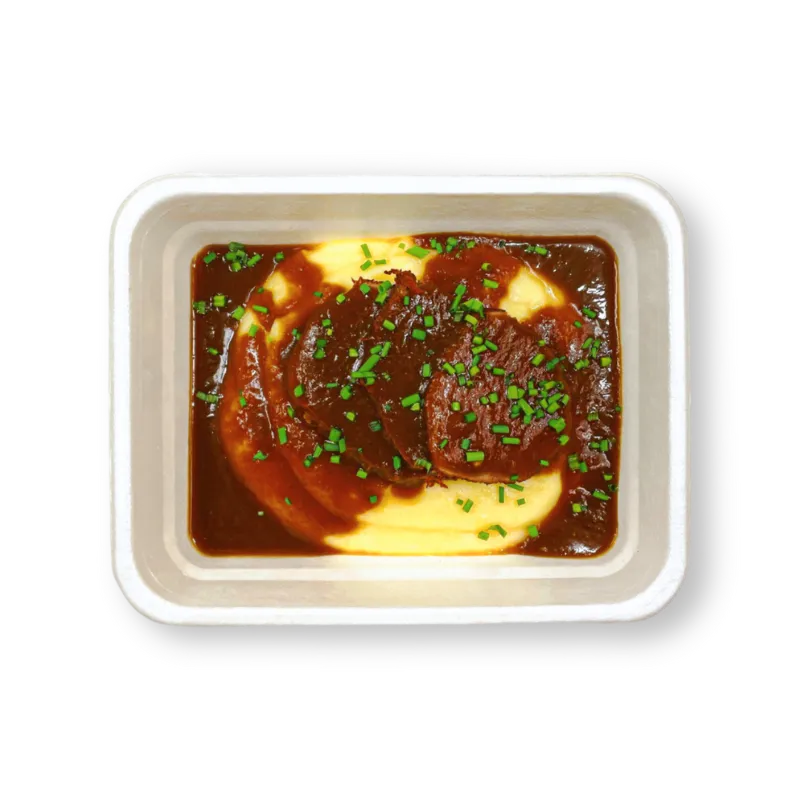 Meal tray with mashed potatoes topped with slices of beef and brown gravy garnished with chopped chives.