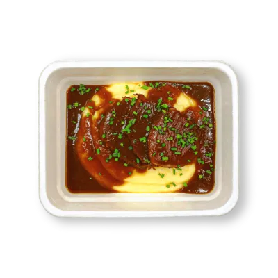 Porce masa s tmavou omáčkou a bramborovou kaší posypané nasekanou zelenou bylinkou v bílé misce.
