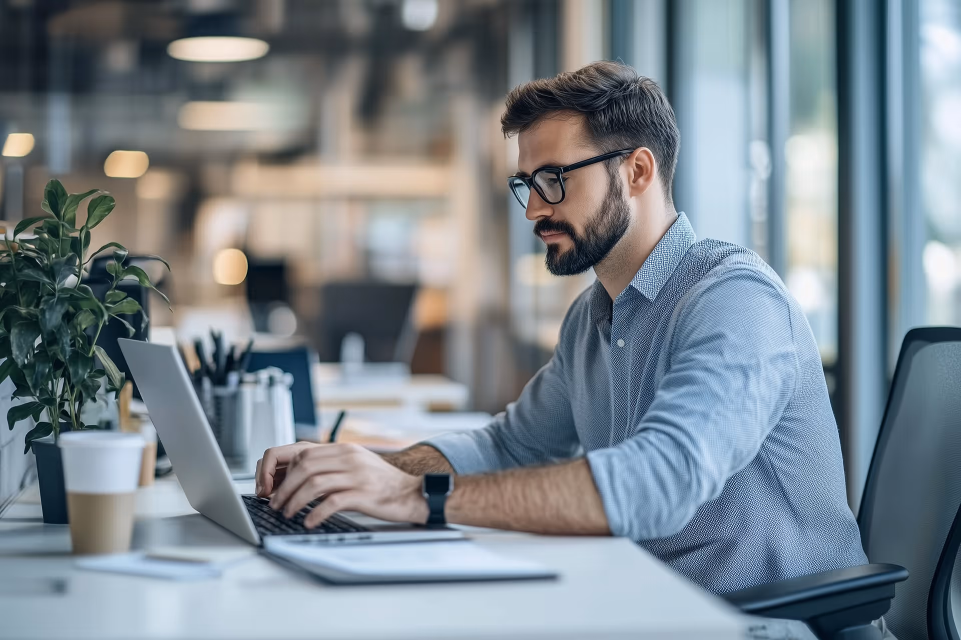 Mitarbeiter in modernem Büro arbeitet konzentriert am Laptop – digitaler Versand vereinfacht Arbeitsabläufe und spart Zeit im Büroalltag.