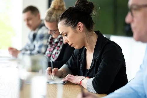 Mitarbeitende sitzen gemeinsam an einem Tisch und schreiben konzentriert mit – das Bild vermittelt Teamgeist, Engagement und die gemeinsame Ausrichtung auf die Unternehmensziele von Postcon.