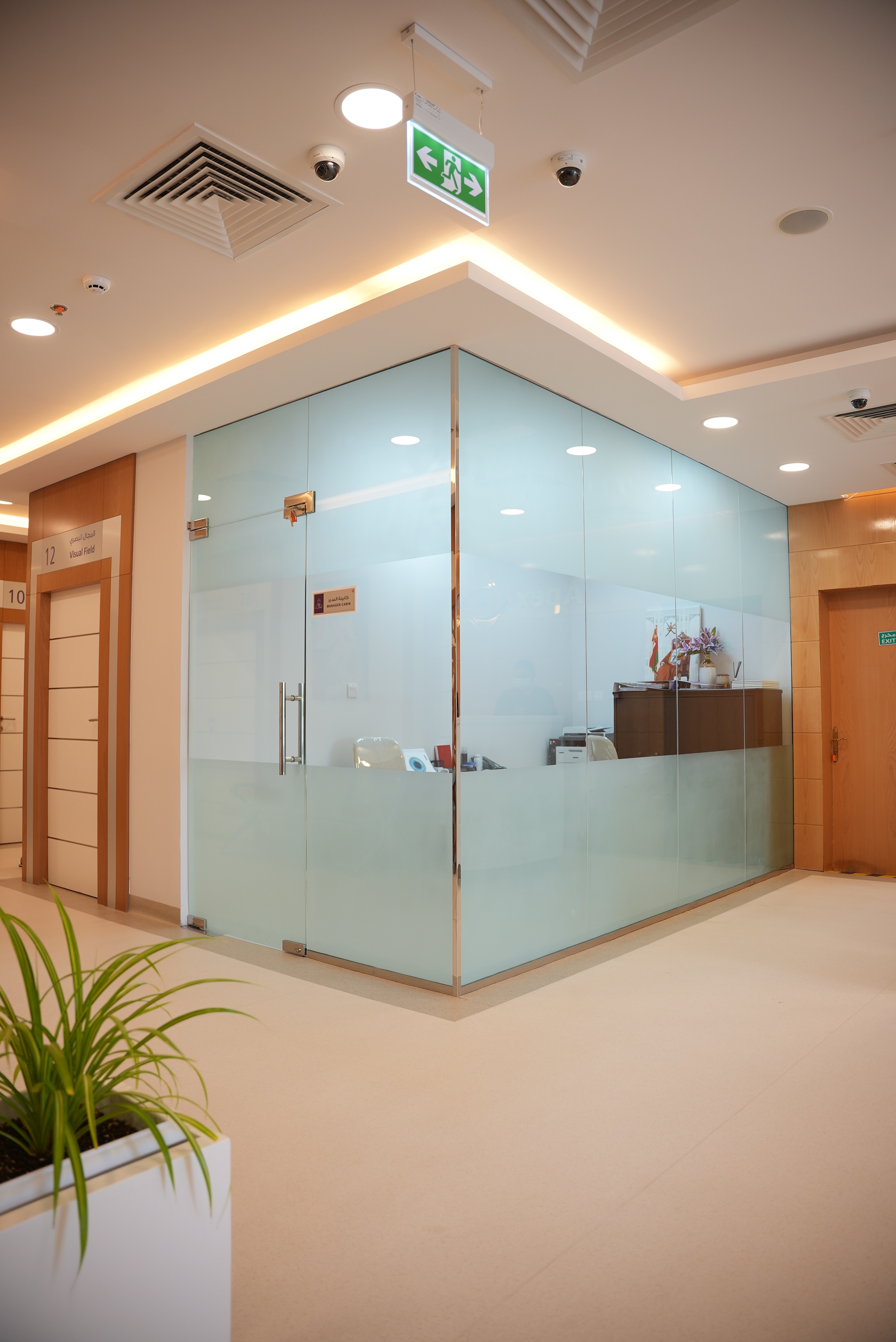 Modern hospital corridor with glass-walled office labeled 'Manager Cabin' and potted plant.