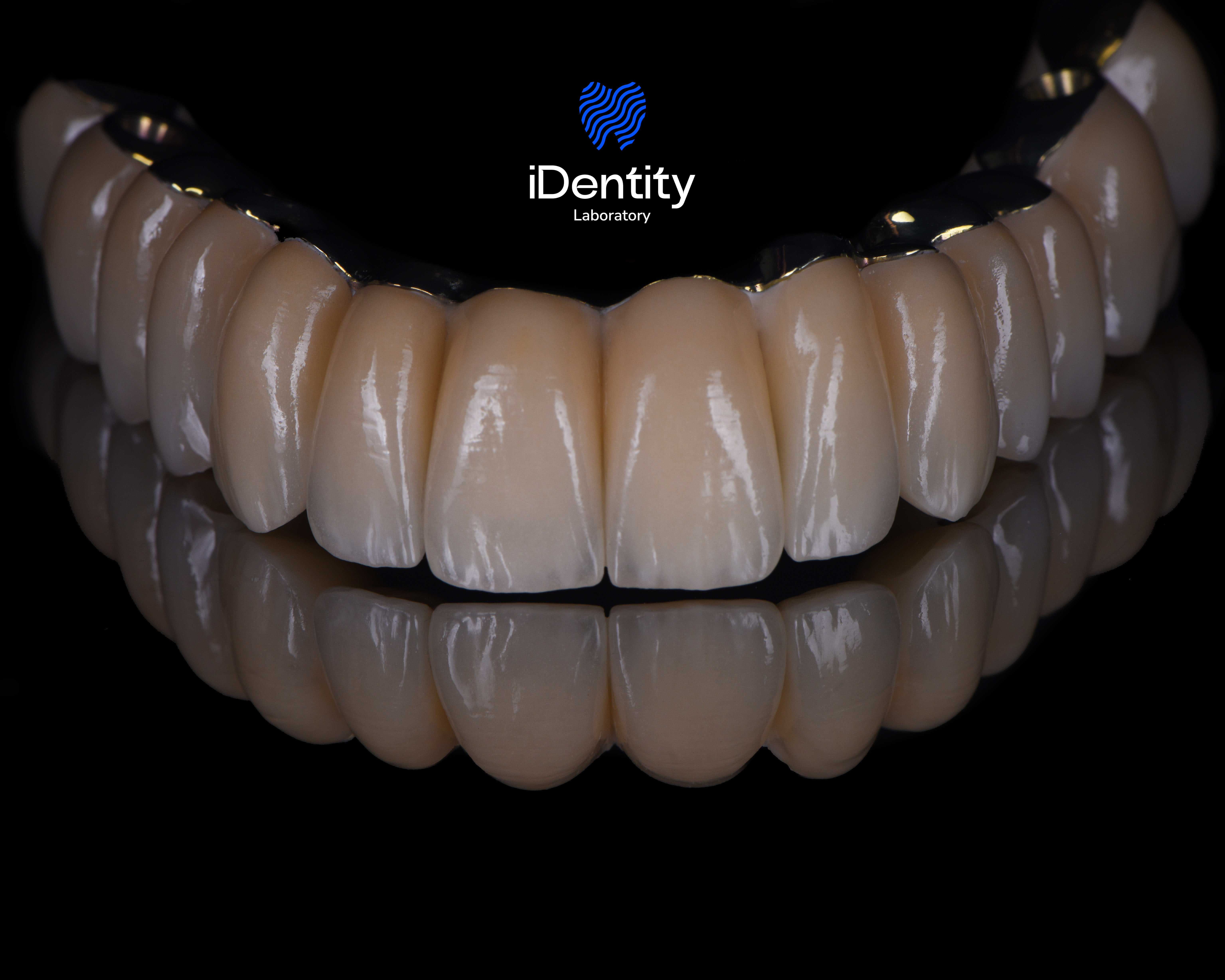 Close-up of a set of artificial teeth with a reflective black background and the iDentify Laboratory logo above.