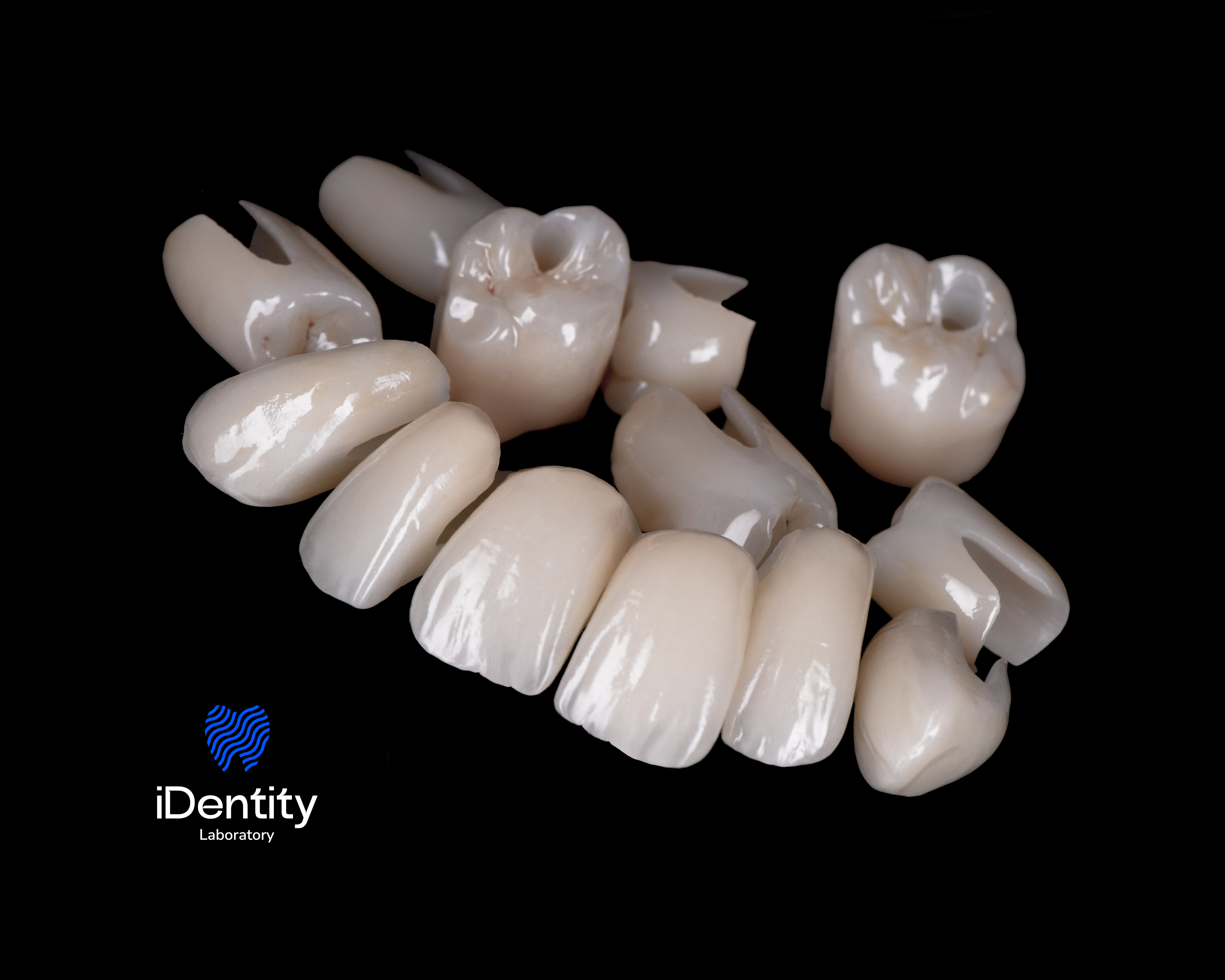Set of dental crowns and veneers arranged on a black background with a blue iDentity Laboratory logo.