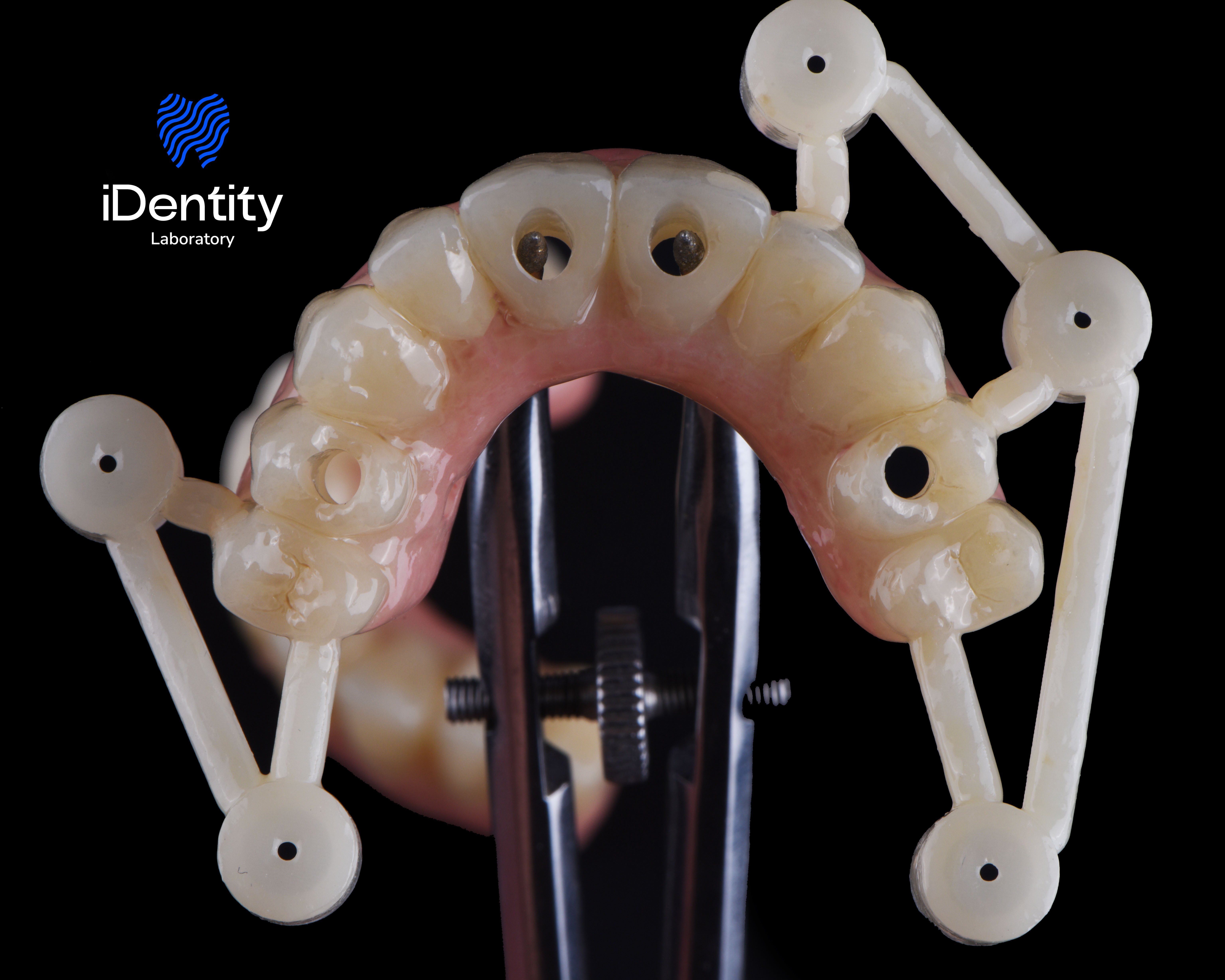 Dental surgical guide with holes for implant placement held by metal clamp against black background.