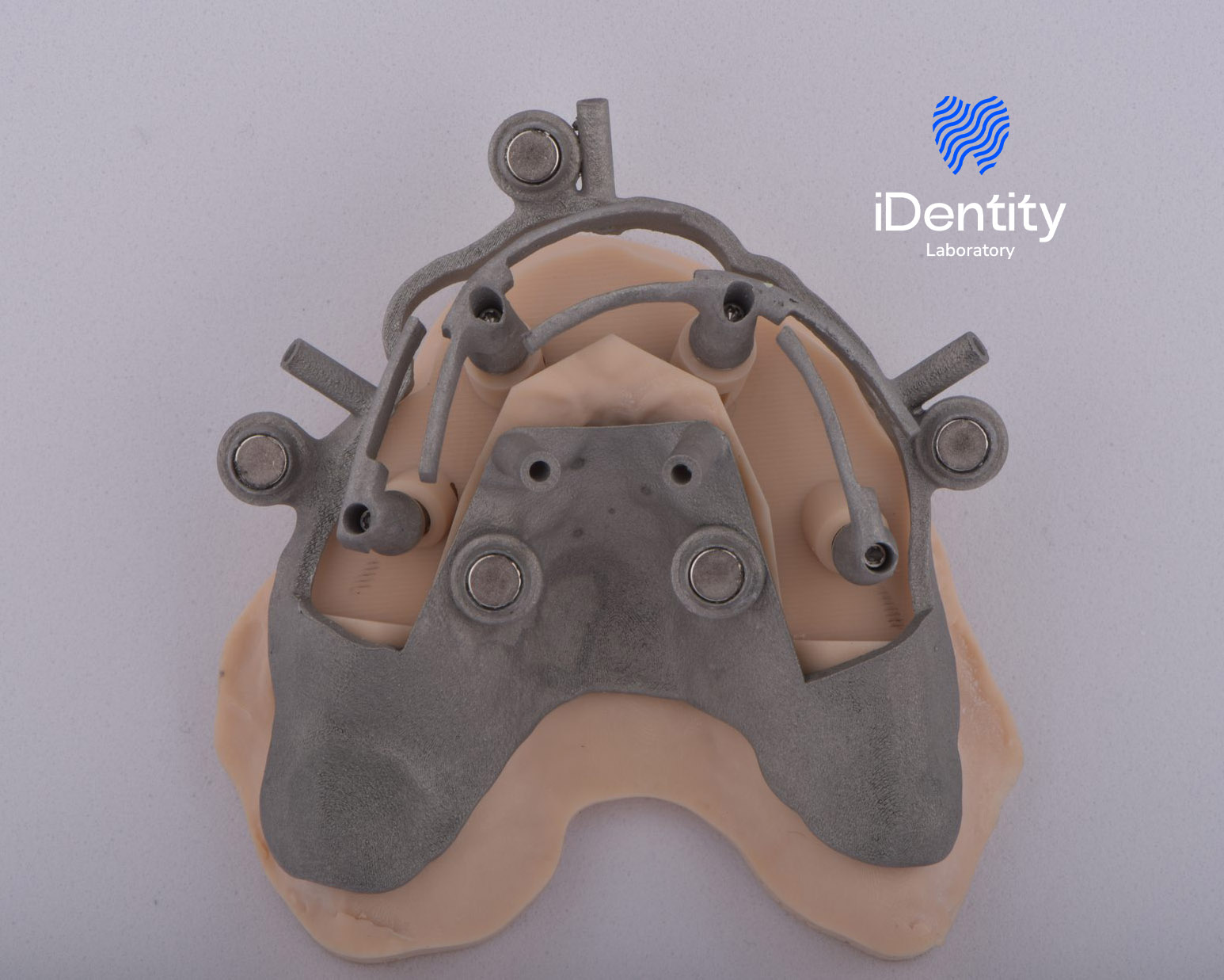 Metal dental implant guide fitted on a pink dental mold on a light gray background with 'iDentity Laboratory' logo.