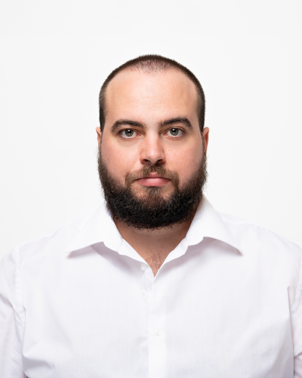 Primo piano di uomo con barba folta e capelli corti, indossa una camicia bianca con sfondo bianco.