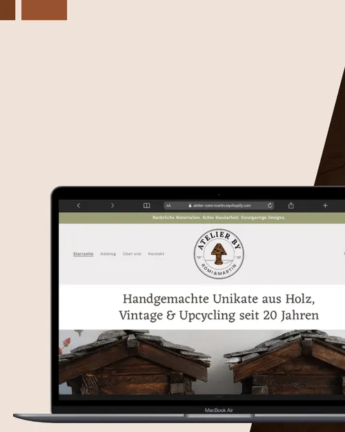 Laptop-Bildschirm zeigt eine Website mit dem Logo Atelier by Romi & Martin und dem Text: Handgemachte Unikate aus Holz, Vintage & Upcycling seit 20 Jahren.