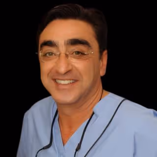 Smiling man wearing glasses and light blue medical scrubs with a stethoscope around his neck.