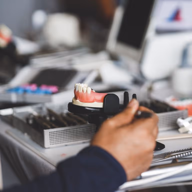 Dental technician working on a partial denture model at a workstation.