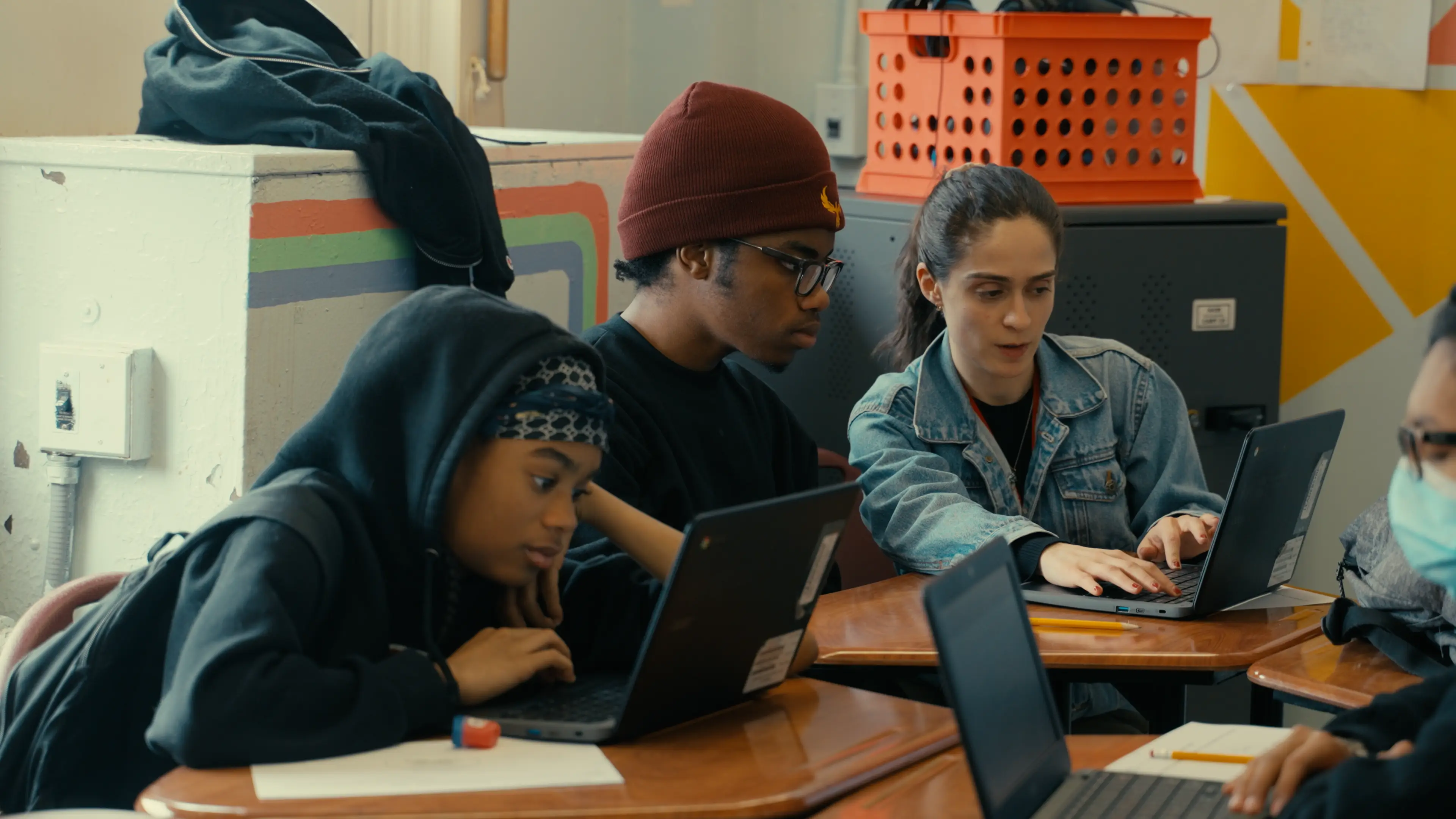Three students working collaboratively on laptops at school desks in a classroom.