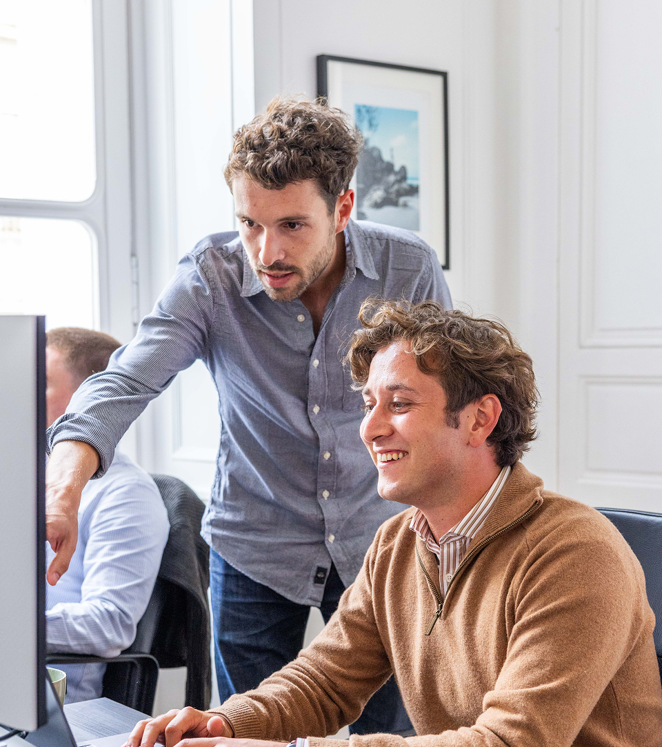 deux personnes de prospilot travaillant devant un ordinateur, l'un sourit et l'autre lui montre quelque chose à l'écran