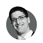 Black and white headshot of a smiling man wearing glasses and a suit.