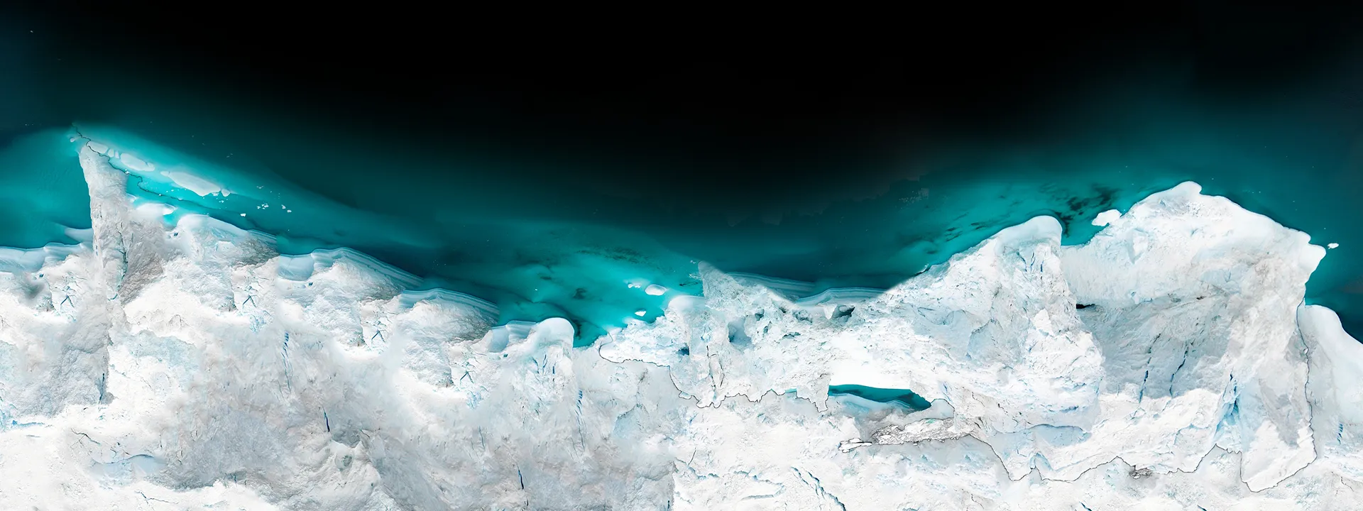 Aerial view of white and blue glacial ice formations bordering a dark blue body of water.