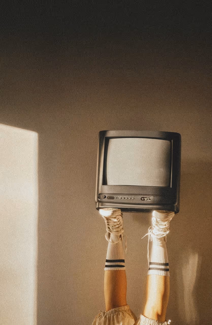 Gambe alzate con calzini bianchi a righe e scarpe da ginnastica che tengono sopra una vecchia televisione.