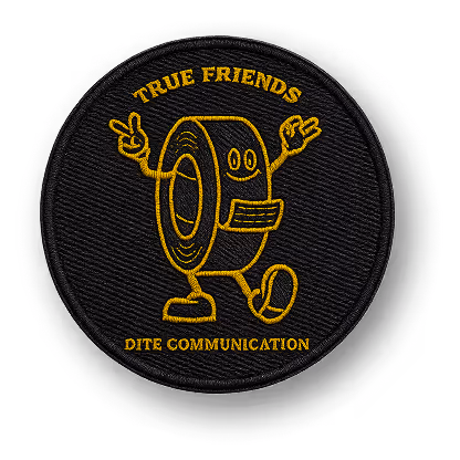 Toppa rotonda nera con ricamo giallo che raffigura un rotolo di nastro adesivo sorridente con braccia e gambe, con la scritta True Friends sopra e Dite Communication sotto.