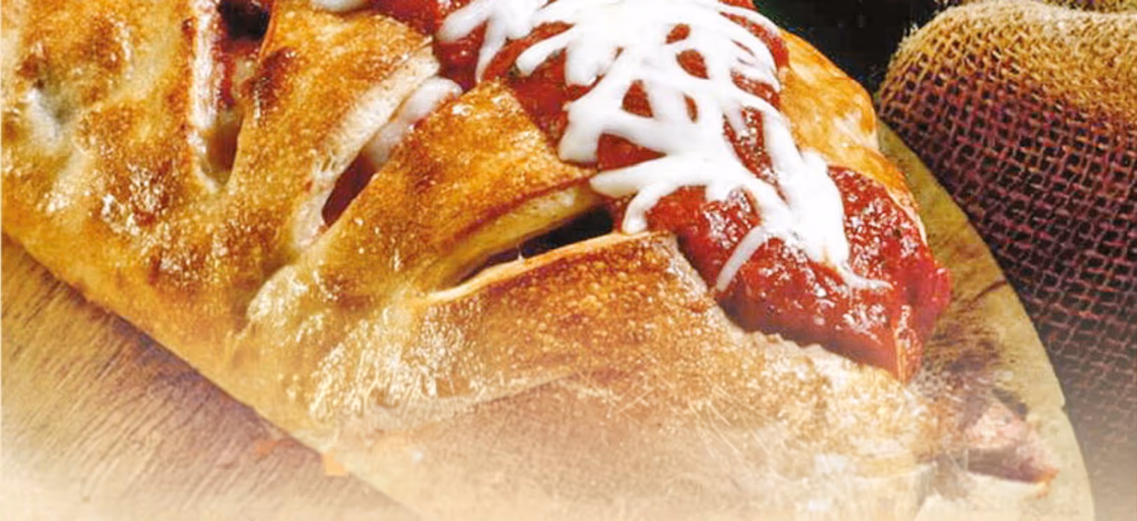 Golden-brown baked pastry topped with tomato sauce and melted white cheese on a wooden surface.