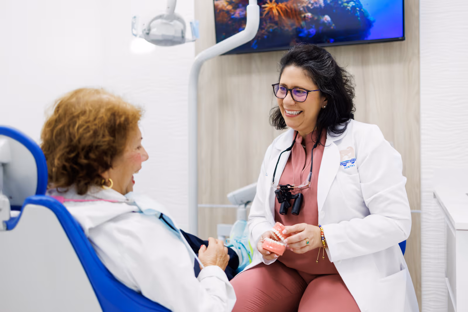 Smiling female dentist explaining dental care to a female patient in a dental office using a teeth model.