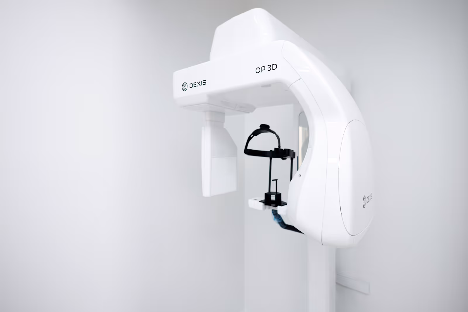 White DEXIS OP 3D dental imaging machine mounted on a white wall in a clinical setting.
